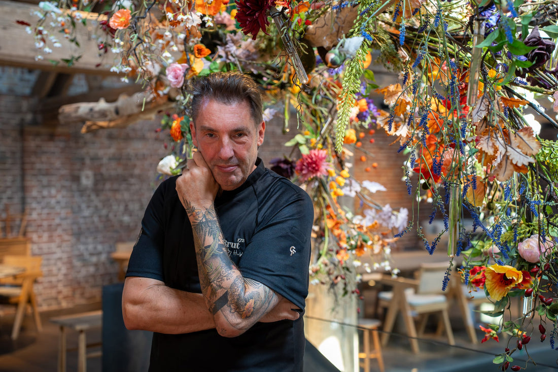 Hans van Wolde met de armen over elkaar onder een installatie van bloemen en takken