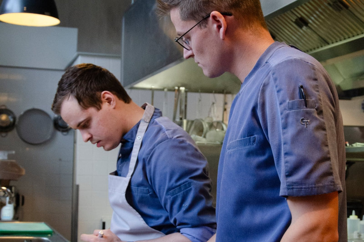 Twee koks in blauwe Wastewear-koksbuizen aan het werk in de keuken